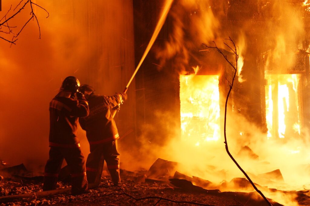 Deux pompiers projettent de l’eau sur un incendie de nuit