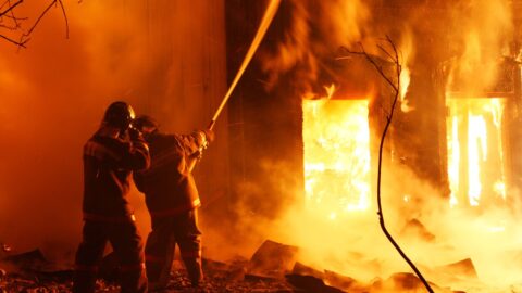 Deux pompiers projettent de l’eau sur un incendie de nuit