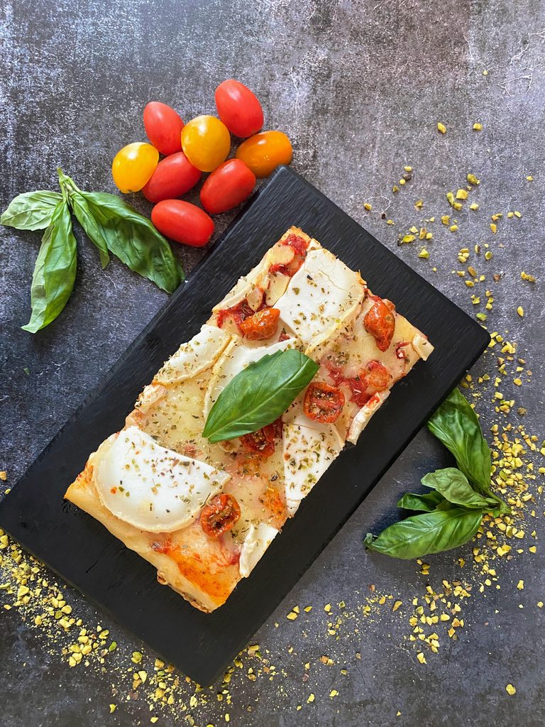 Une part de pizza rectangulaire garnie de fromage, tomates et basilic illustre le service à la coupe proposé le midi chez Casale Taglio.