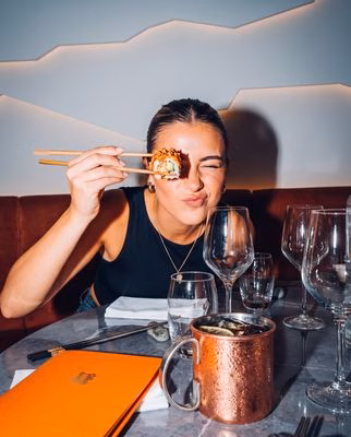 Une convive tenant un sushi avec des baguettes chez NETA